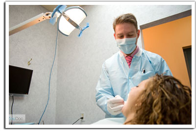 The image shows a dental professional wearing a face mask and gloves, standing next to a patient who appears to be receiving dental care, with a focus on oral health and hygiene.