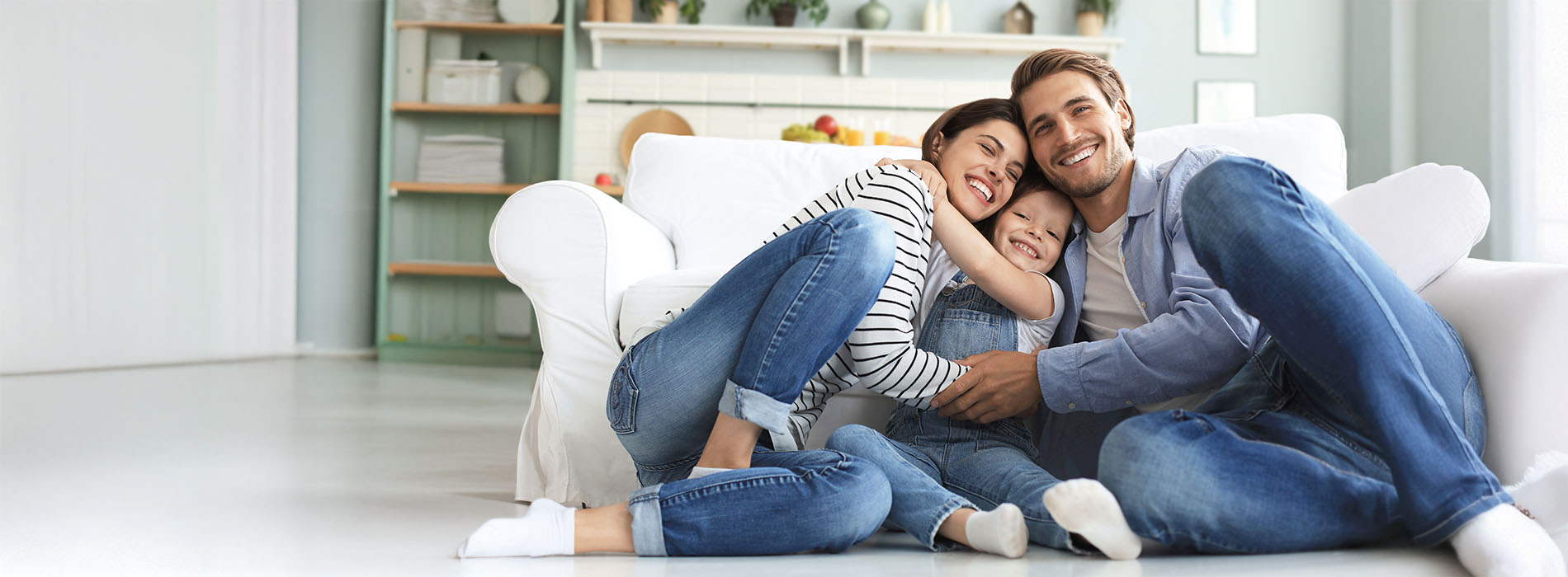 A family of four sitting on a couch in a living room, with the father embracing his wife and their two children beside them.