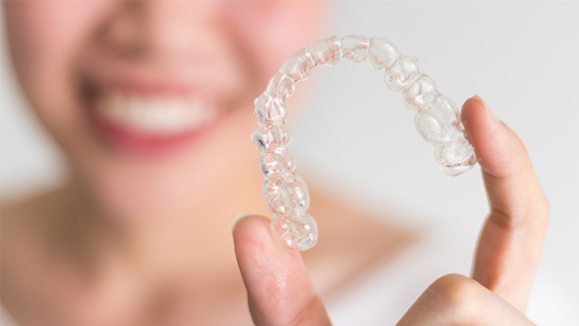 Clear plastic aligner tray held by smiling person s hand.