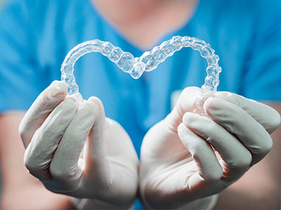 A dental professional s hands holding a clear plastic heart-shaped object with a transparent smile line, symbolizing dental care or dental implants.