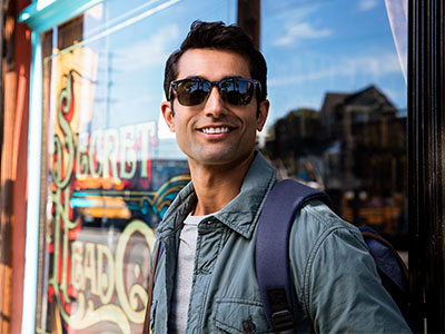 A man in sunglasses and a jacket stands confidently against a storefront window with a sign that reads Sweet Treats.
