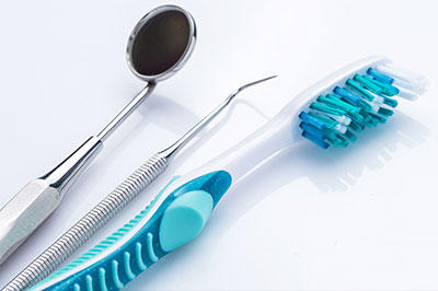 An assortment of dental tools including a toothbrush with blue bristles, a dental mirror, and a pair of tweezers on a white background.