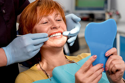 The image shows a woman sitting in a dental chair, receiving dental care with a smile on her face, while holding a blue toothbrush and wearing a red headband.