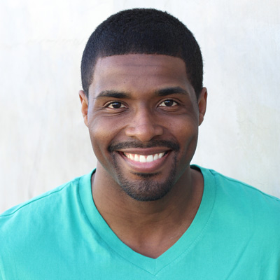A man and woman are smiling and embracing each other outdoors with mountains in the background.
