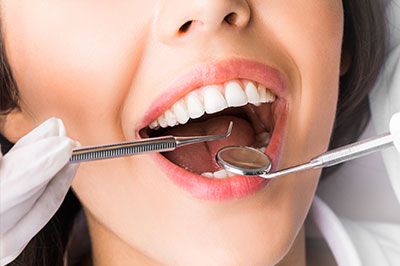 A woman with a wide smile has her teeth worked on by a dental professional using specialized tools.