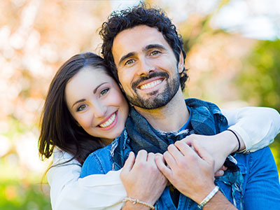 A man and woman embrace each other in a joyful pose against a blurred outdoor background.