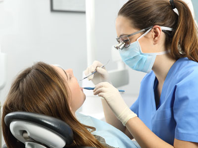 A dental professional, wearing protective gear and using dental tools on a patient s teeth during an appointment.