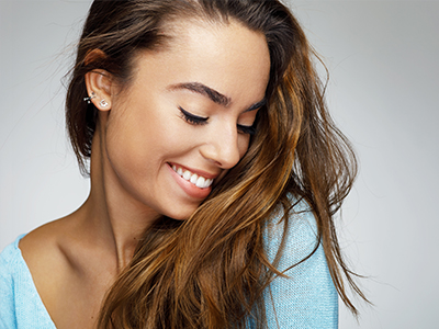 A woman with long hair, smiling, against a plain background.