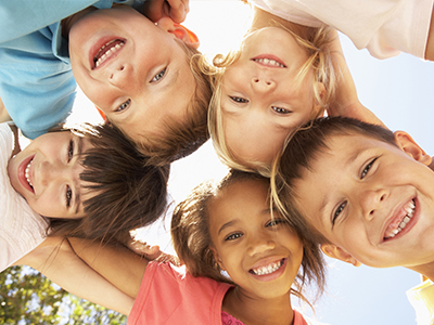 The image shows a group of children of various ages and ethnicities smiling at the camera from different angles.