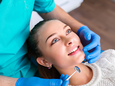 The image shows a dental professional performing a dental procedure on a patient, with the patient smiling and wearing a blue surgical gown.