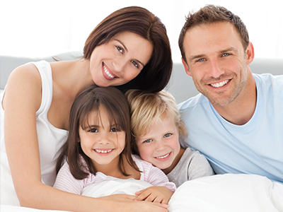 A family of four adults and two children posing together on a bed with smiles, likely for a holiday greeting or similar occasion.