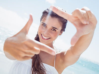 A woman taking a selfie with her hand extended towards the camera, set against a beach backdrop.